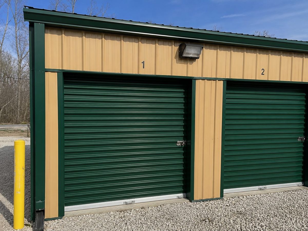 Close-up of storage units 1 and 2 with green roll-up doors, tan siding, and security lighting at U.S. 60 West Storage LLC
