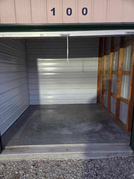Interior view of storage unit 100 showing a clean concrete floor and roll-up door partially visible